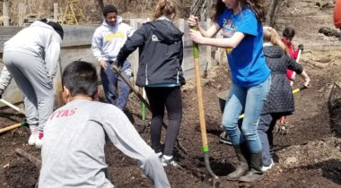 Seven young people working with shovels and rakes in an outdoors space.